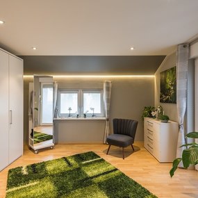 Modernes Schlafzimmer mit großem Kleiderschrank, gemütlichem Sessel und viel Tageslicht.