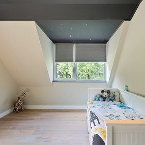 Helles Kinderzimmer im Dachgeschoss mit Bett, Kuscheltieren, Fenster und Holzfußboden.