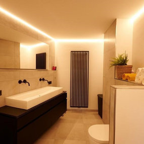 Modernes Badezimmer mit großer Spiegelwand, LED-Beleuchtung und stilvollem Waschtisch.