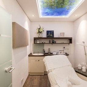 Moderner Behandlungsraum für Kosmetik mit Liege, Holzfußboden und Naturmotiv an der Decke.