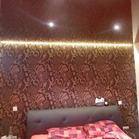 Schlafzimmer mit gemusterter Tapete, modernem Bett und indirekter LED-Beleuchtung.